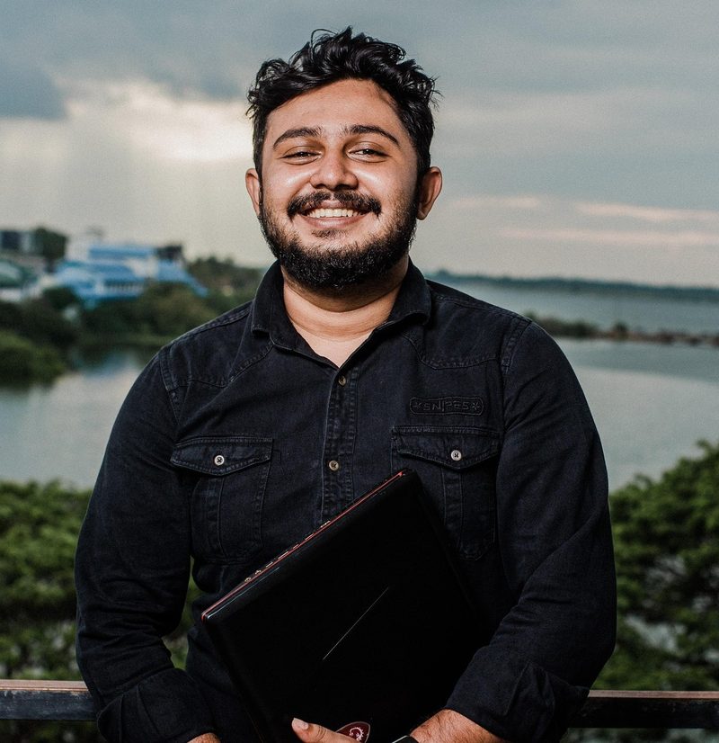 A smiling man holding a laptop on a terrace above the water